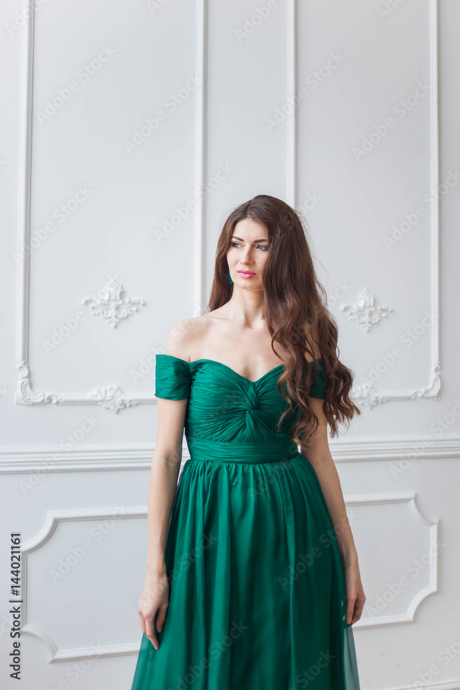 beautiful brunette girl with curly hair in the green dress in Studio with white walls looks into the camera beautiful brunette girl with curly hair in the green dress in Studio with white walls looks into the camera