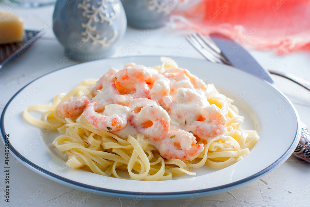 Italian pasta fettuccine in a creamy sauce with shrimp close-up on a plate. horizontal