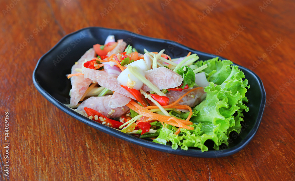 Thai sour pork sausage salad in black plate on wood table