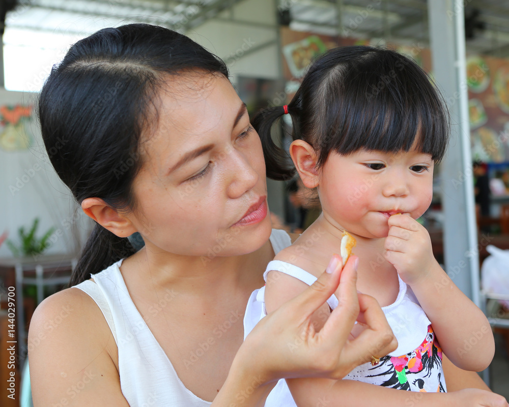 Asian mother and her baby little girl eating a chicken wing Asian mother and her baby little girl eating a chicken wing