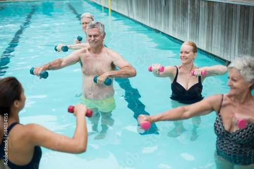 Senior swimmers and instructor lifting dumbbells  © WavebreakMediaMicro