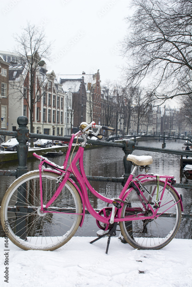 Bright pink bike on the bridge near the canal in Amsterdam in winter