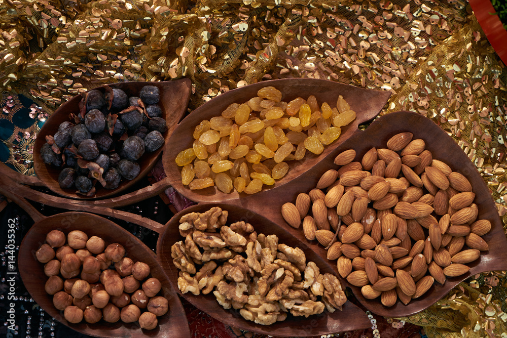 Obraz premium Large collection of nuts, seeds and dried fruits in brown wooden bowls isolated on a golden background