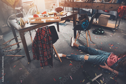 Cropped shot of drunk young woman lying on floor in messy room after party photo