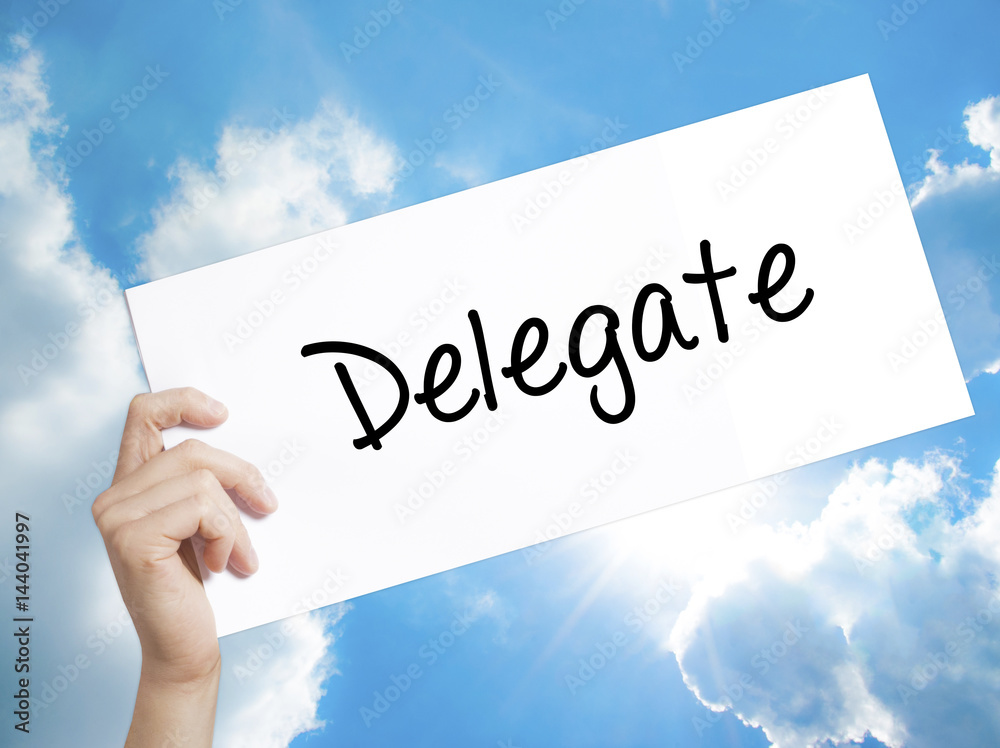 Delegate Sign on white paper. Man Hand Holding Paper with text. Isolated on sky background Delegate Sign on white paper. Man Hand Holding Paper with text. Isolated on sky background