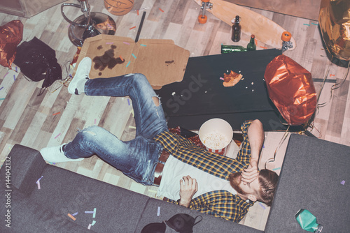 Photography drunk bearded man lying on floor in messy room after party