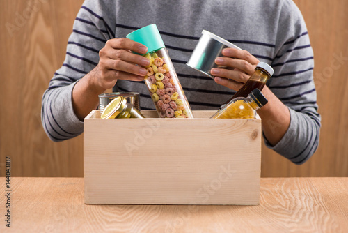 Volunteer with donation box with foodstuffs on wooden background © makistock