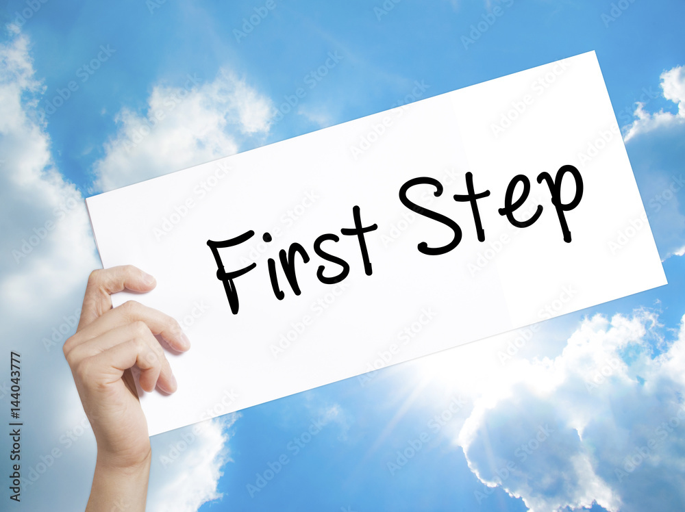 First Step Sign on white paper. Man Hand Holding Paper with text. Isolated on sky background First Step Sign on white paper. Man Hand Holding Paper with text. Isolated on sky background