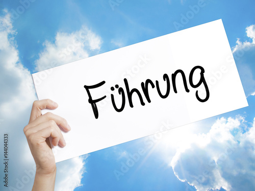 Fuhrung (Leadership in German) Sign on white paper. Man Hand Holding Paper with text. Isolated on sky background.