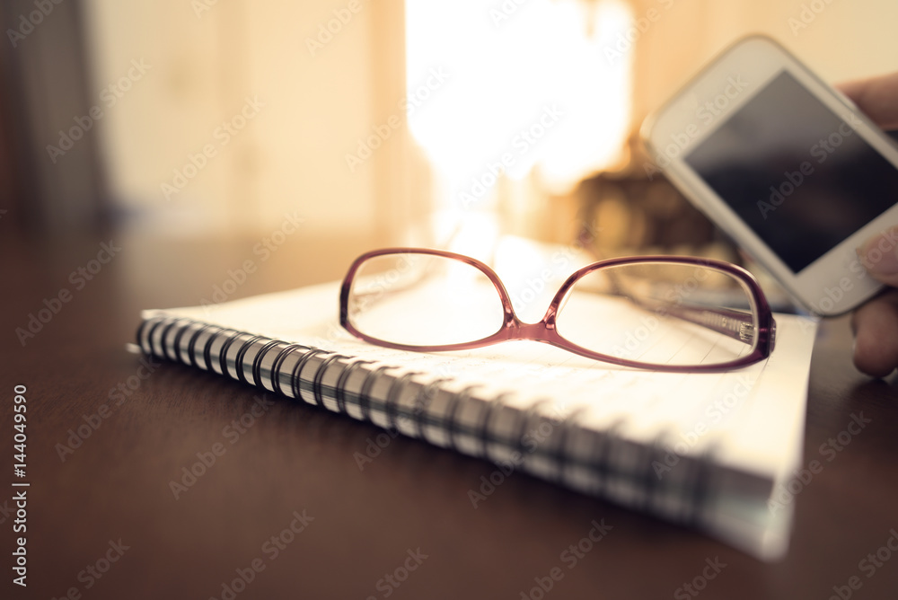 Glasses notebook smart phone and pen on brown wooden desk in home office Glasses notebook smart phone and pen on brown wooden desk in home office