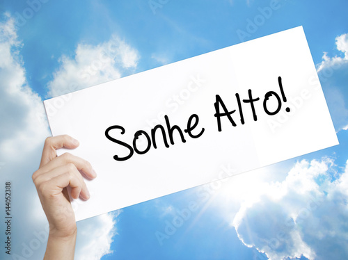 Sonhe Alto! (Dream Big in Portuguese) Sign on white paper. Man Hand Holding Paper with text. Isolated on sky background photo
