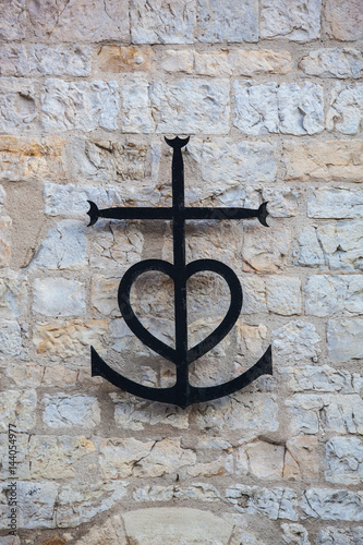 Black camargue cross on stone wall, closeup. Camargue symbol faith, hope and love, France