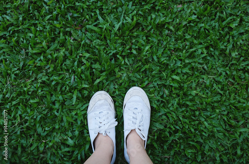 Selfie of feet in sneakers shoes on green grass background with copy space, spring and summer concept