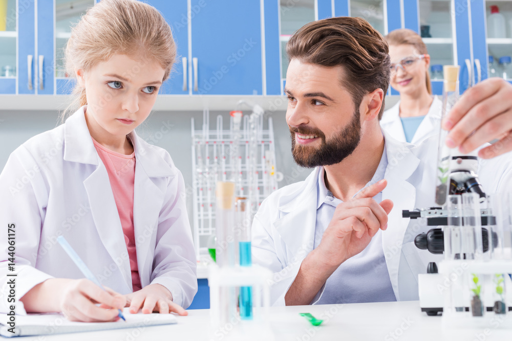 Obraz premium Smiling bearded teacher and serious little student making experiment in lab