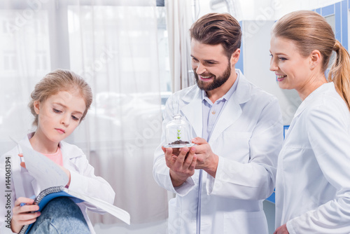 Smiling teachers scientists and serious student looking at green plant in laboratory