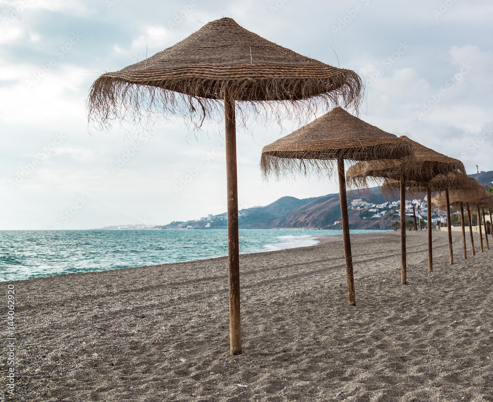 Straw parasols on empty beach. Nerja, Spain