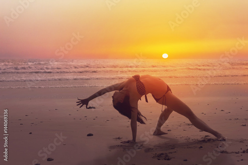 Woman doing a yoga pose on the beach at sunset