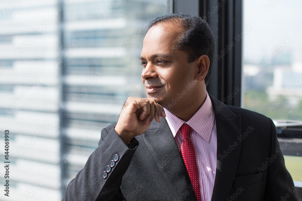 Smiling Indian businessman looking out of window Smiling Indian businessman looking out of window