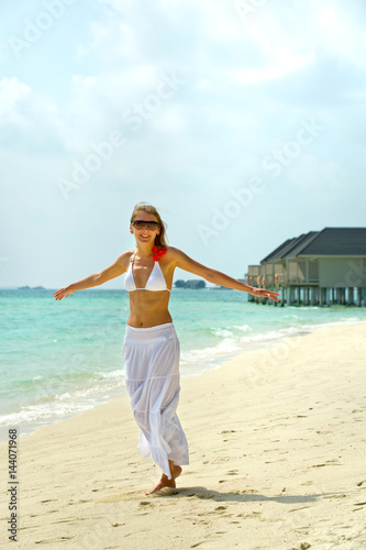 Happy young woman dances on the beach. Happy lifestyle. White sand  blue sky