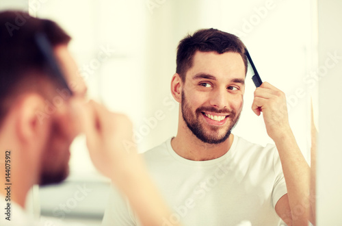 happy man brushing hair with comb at bathroom