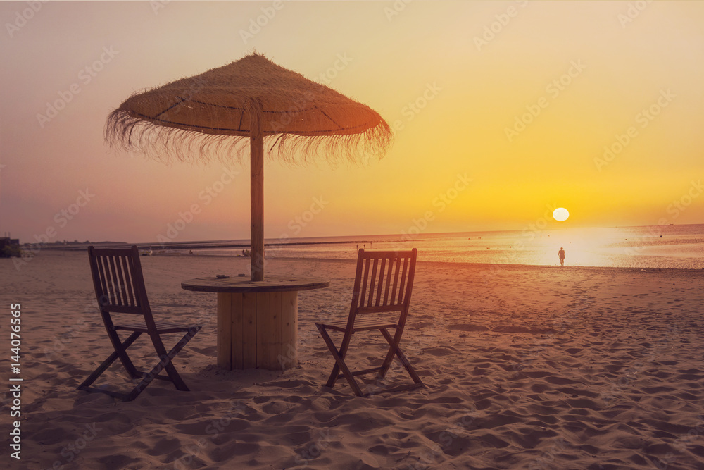Wooden table and chairs with umbrella on the beach at sunset