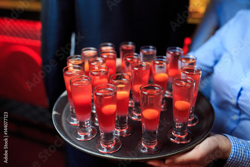 Glasses with red cocktails on a tray in the hands of the waiter