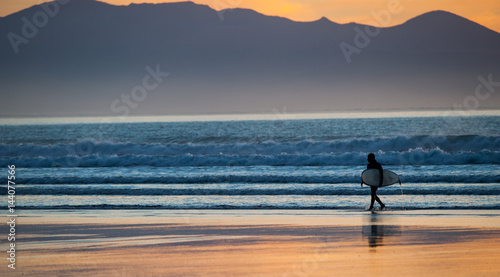 Photography Surfer with surfboard walking out of the ocean at sunset