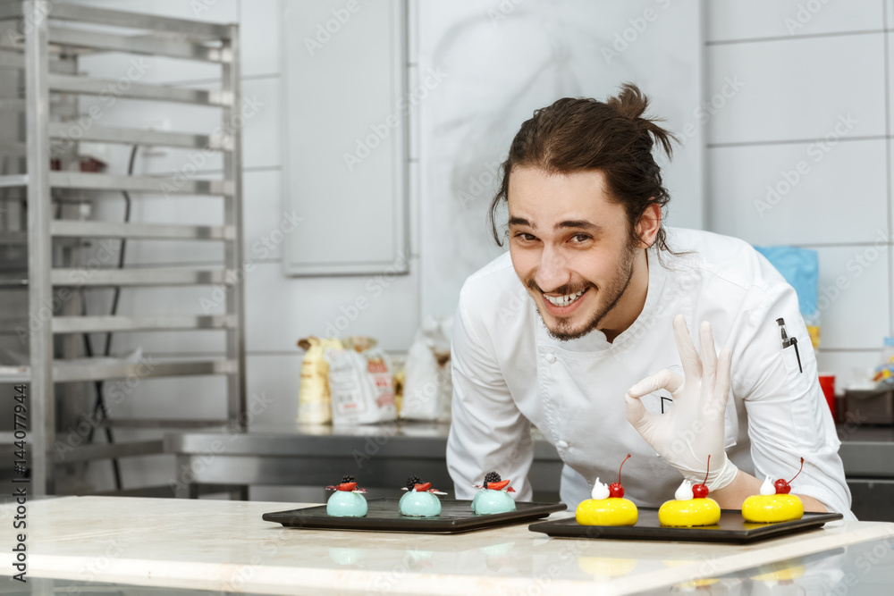 Cheerful chef posing with his cakes at the kitchen Cheerful chef posing with his cakes at the kitchen