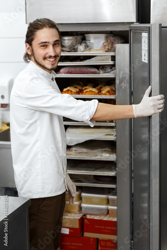Young chef smiling near an open refrigerator
