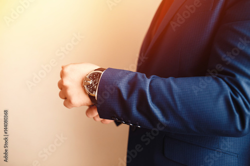 Businessman in blue suit puts the clock on the background of sunlight. Conception is businessman, business meeting, negotiations, fiance