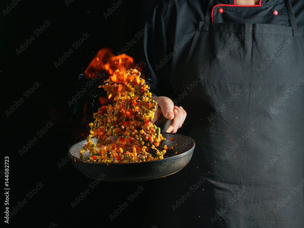 Cooking of vegetable mix stew with tossing on a hot frying pan in the tongues of flame. Colorful grains of corn and peas, asparagus and sweet peppers. Cooking of vegetable mix stew with tossing on a hot frying pan in the tongues of flame. Colorful grains of corn and peas, asparagus and sweet peppers.