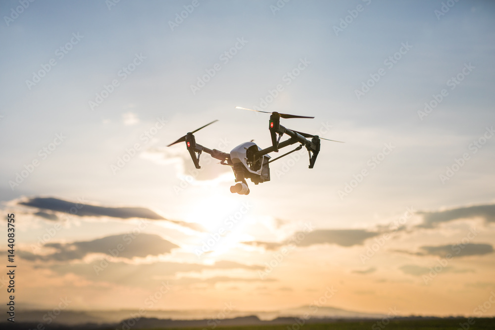 silhouette of flying drone in glowing red sunset sky - obrazy, fototapety, plakaty 