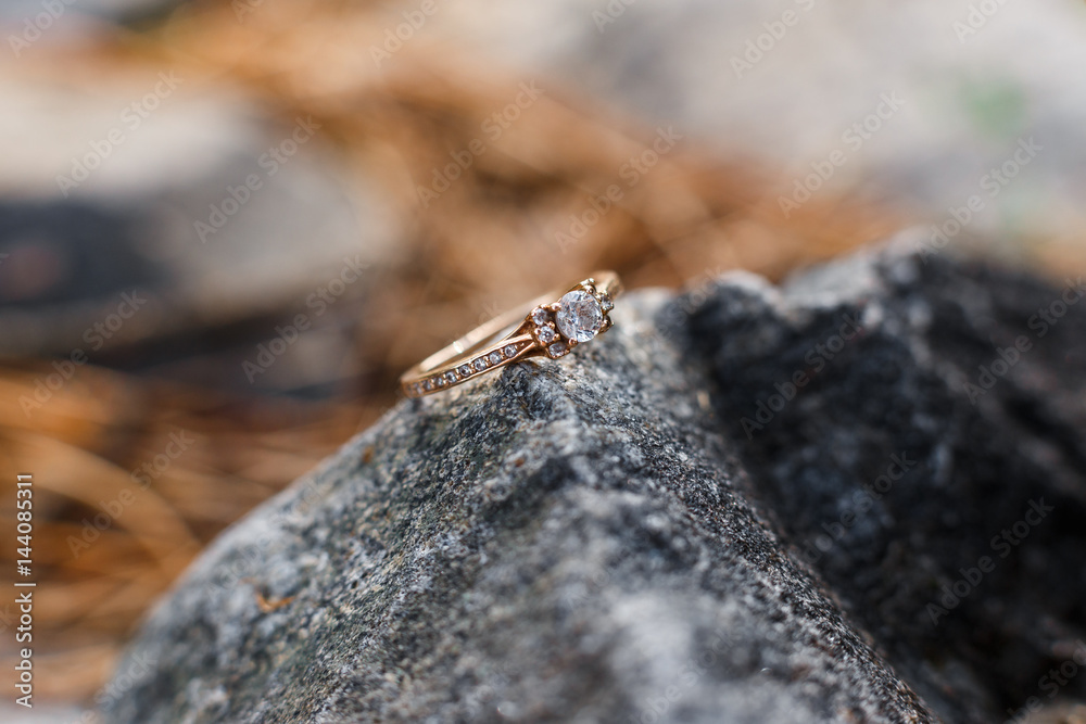 Gold wedding rings with a lot of gemstones lying on the grey stone and shining in the sun rays. Jewelry made of yellow gold