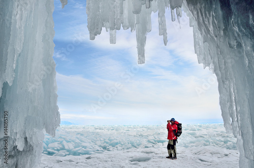 Турист фотографирует ледяные торосы на озере Байкал на фоне ледяного грота
