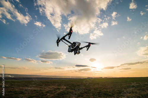 White drone with digital camera flying in sky over field on sunset
