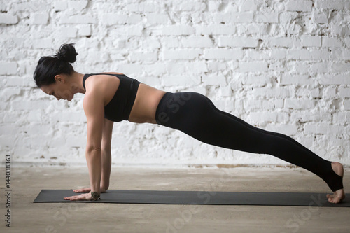 Middle aged yogi attractive woman practicing yoga concept, standing in Push ups, press ups exercise, phalankasana, Plank pose, working out wearing black sportswear, full length, white loft background
