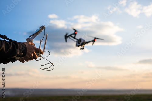 Fototapeta Naklejka Na Ścianę i Meble -  Demonstration of .copter Man controls quadrocopter flight. Flying the copter over a field over sunset sky. Remote control in a man's hands.