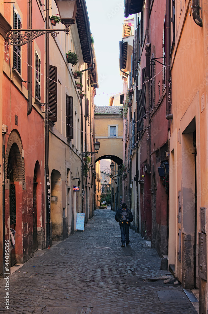 A lonely tourist with a backpack walks along a narrow long street. Rome, Italy