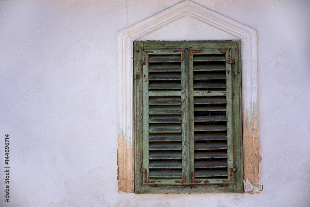 Old green window with closed wooden shutters on an old white masonry