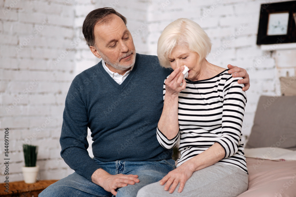 Senior woman blowing her nose near husband