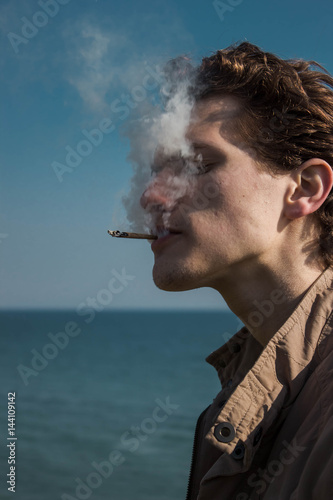 Young man smoking cannabis on the sea background