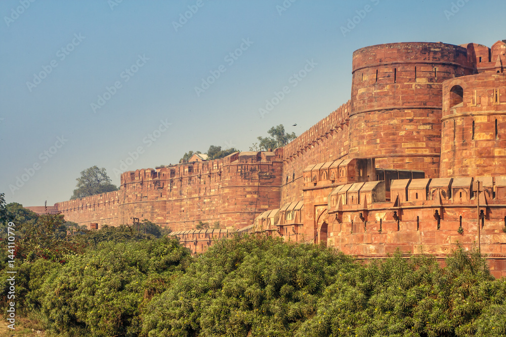 View of the Agra Fort with a blue sky and green bushes on the front. Agra Fort is a historical fort in the city of Agra in India. It is also a UNESCO World Heritage site and is about 2.5 km northwest