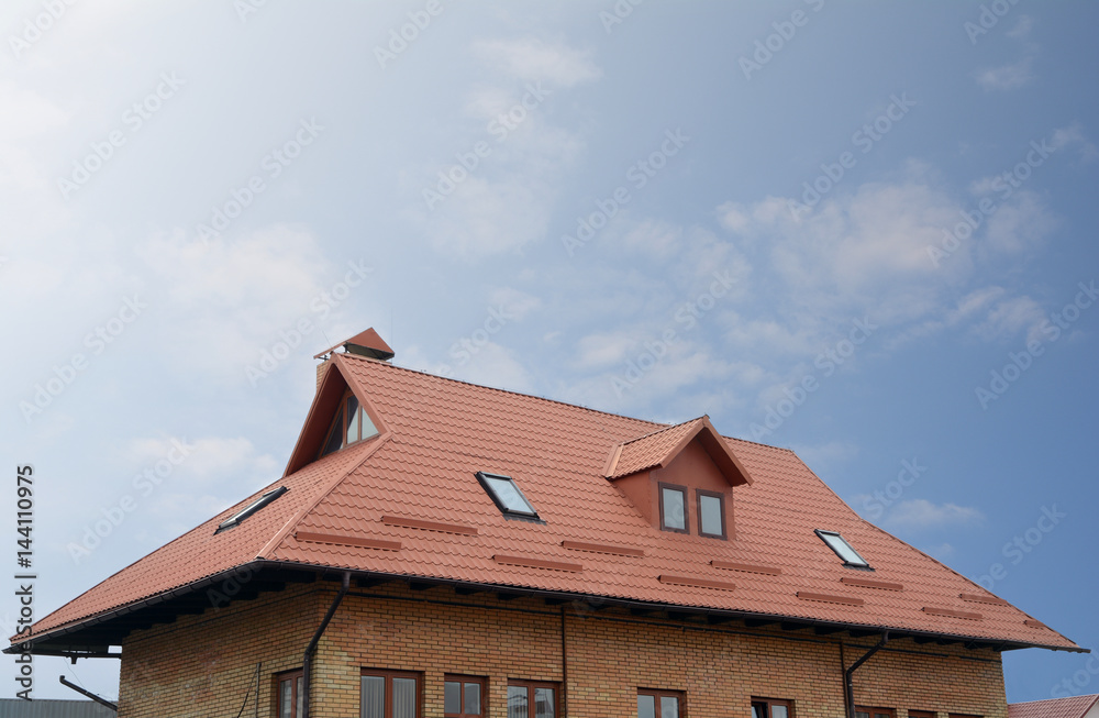 Metal roofing construction. House with a mansard of red brick and skylight windows. Rain gutter and snow guard. Chimney coaxial.