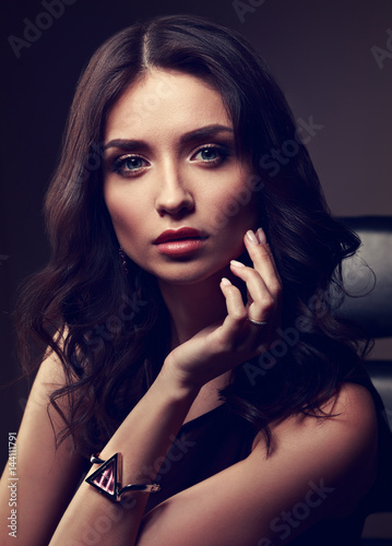 Sexy young makeup model posing on dark shadow background in fashion trendy watch on the hand. Toned art closeup portrait of beautiful woman