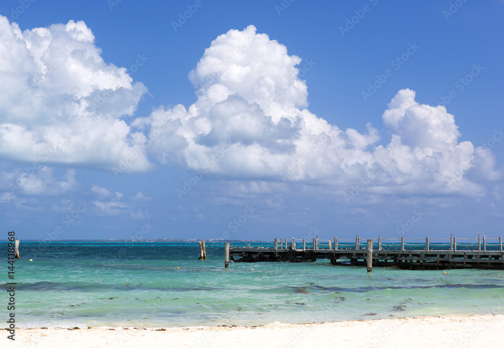Sea side view on the Caribbean sea shore. Long wooden pier, cloudy sky. Turquoise water.