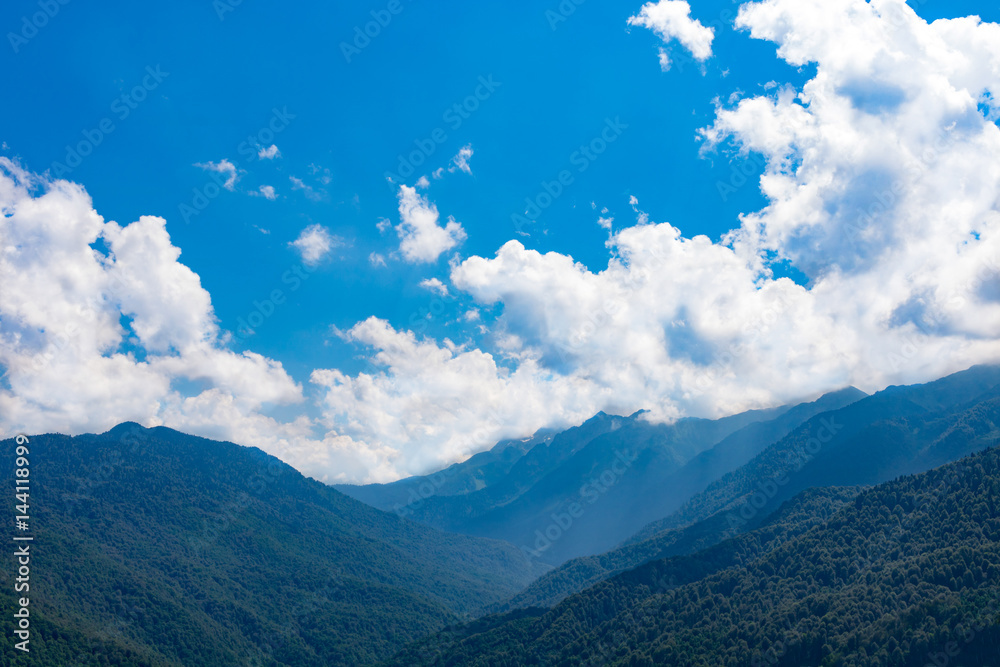 Mountains and clouds in a bright blue sky.