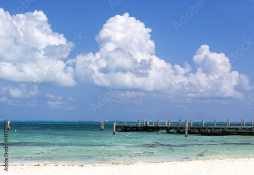 Sea side view on the Caribbean sea shore. Long wooden pier  cloudy sky. Turquoise water.