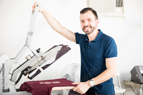 Foto Handsome worker using a serigraphy press on a print shop