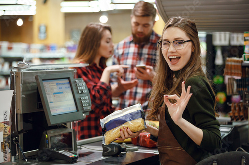 Cashier woman on workspace make okay gesture.