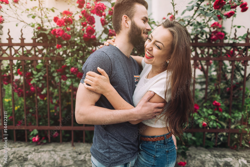 Beautiful and stylish couple of young woman and bearded man near the roses in summer of sunny day. Beautiful and stylish couple of young woman and bearded man near the roses in summer of sunny day.